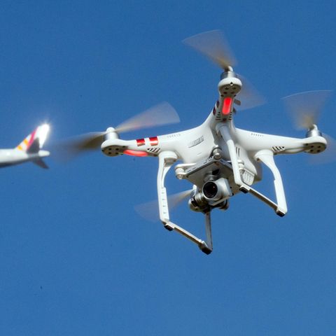 In der Umgebung eines deutschen Flughafens: Eine private Drohne fliegt in knapp zehn Metern Flughöhe über einem Garten, als in weiter Entfernung ein Flugzeug zu sehen ist.