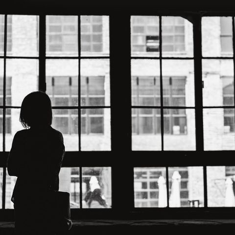 Einsamkeit: Frau steht vor einem großen Fenster.