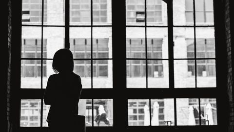 Einsamkeit: Frau steht vor einem großen Fenster.