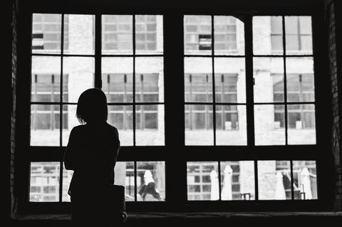 Einsamkeit: Frau steht vor einem großen Fenster.