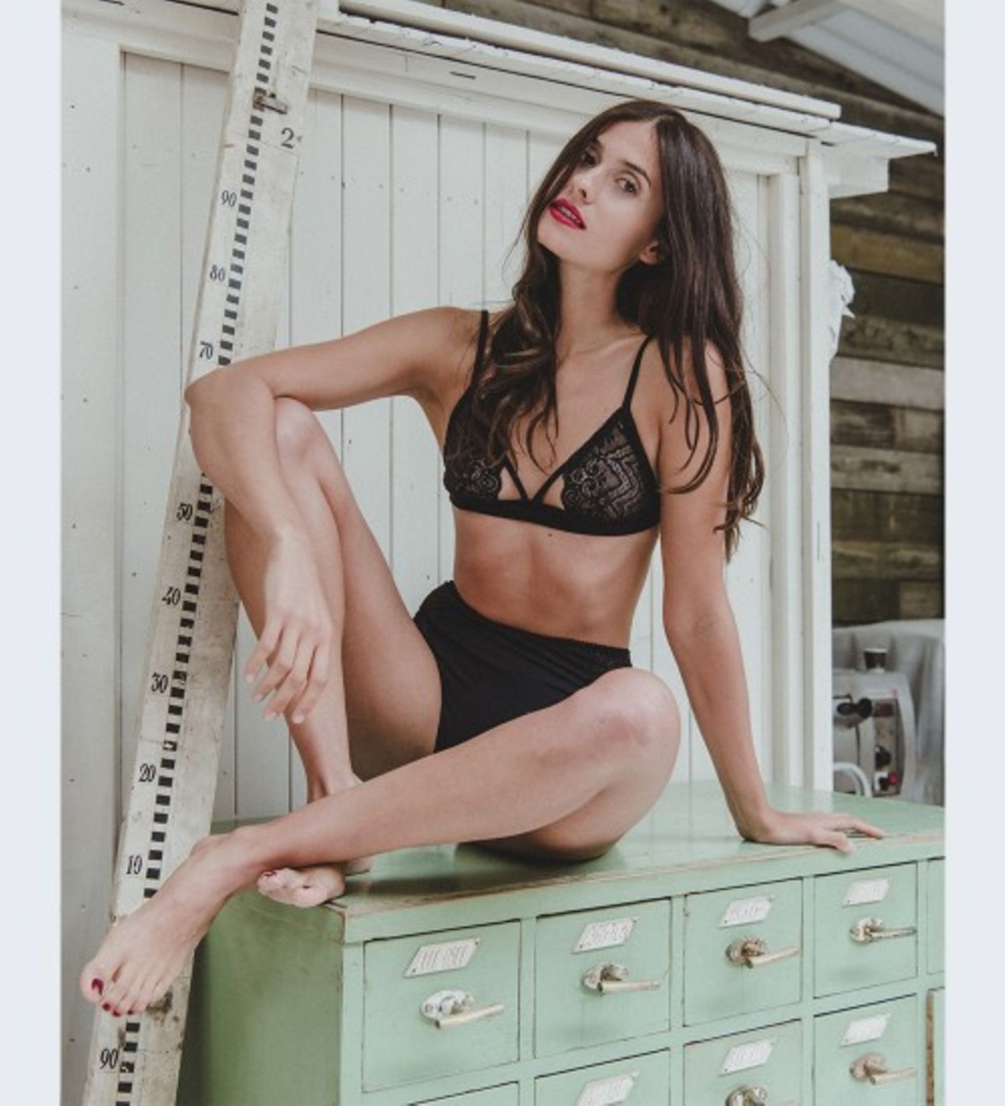 Frau in schwarzer Unterwäsche sitzt auf Kommode.