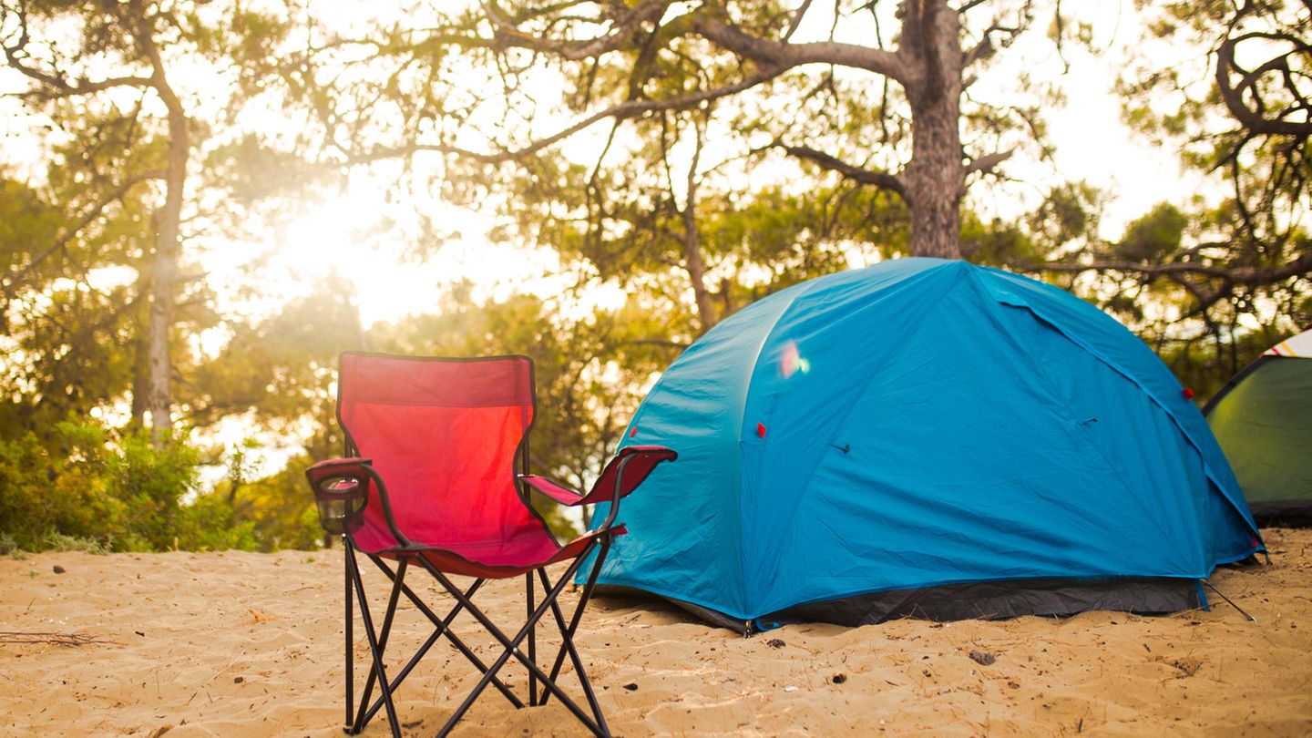 Roter Campingstuhl und blaues Zelt im Wald.