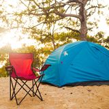 Roter Campingstuhl und blaues Zelt im Wald.
