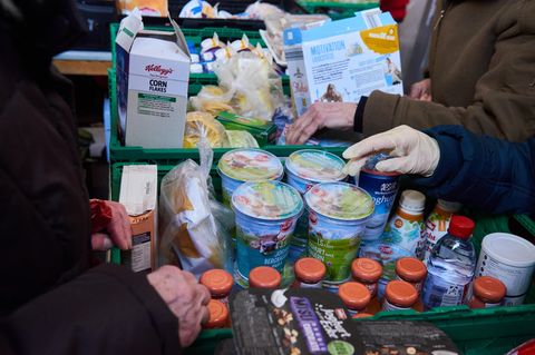 Hände fassen nach abgepacktem Joghurt, Soßen und Cornflakes in Körben der Berliner Tafel