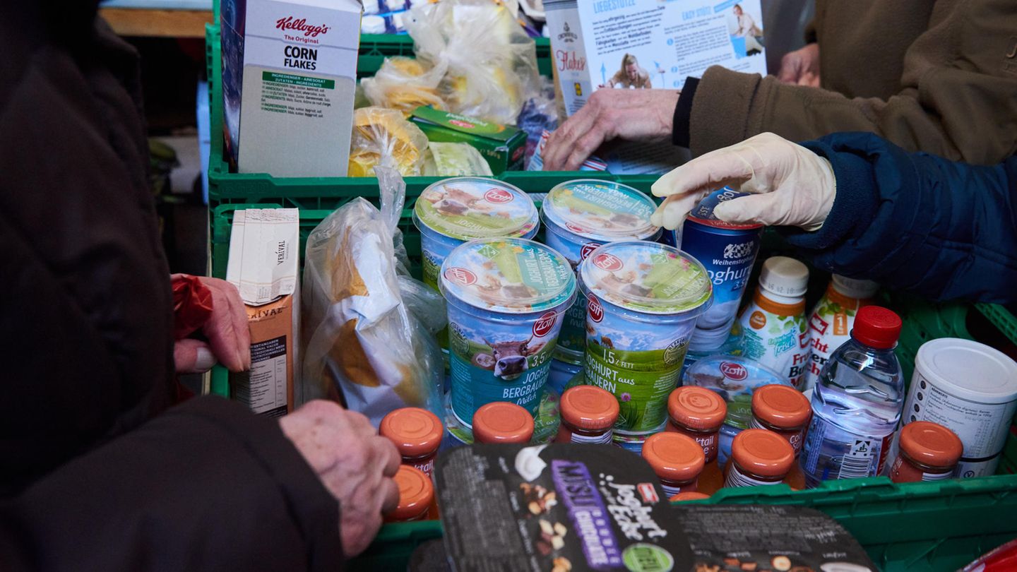 Hände fassen nach abgepacktem Joghurt, Soßen und Cornflakes in Körben der Berliner Tafel