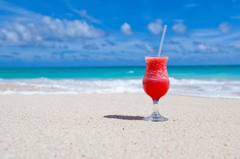 Ein Cocktailglas steht an einem weißen Sandstrand