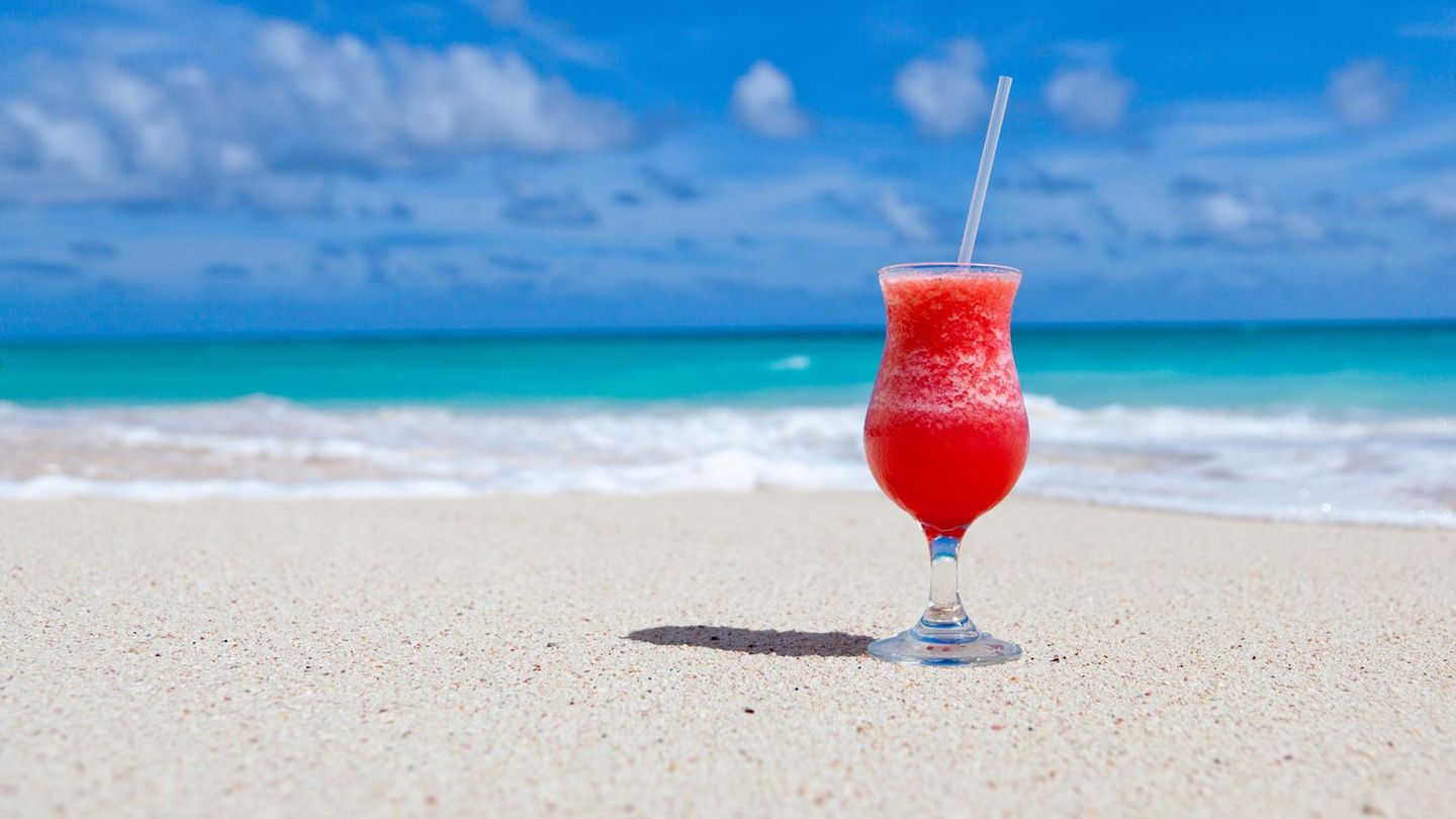 Ein Cocktailglas steht an einem weißen Sandstrand