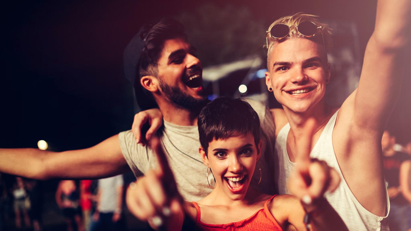 Festivalstimmung. Zwei Männer und eine Frau lachen und tanzen gemeinsam.