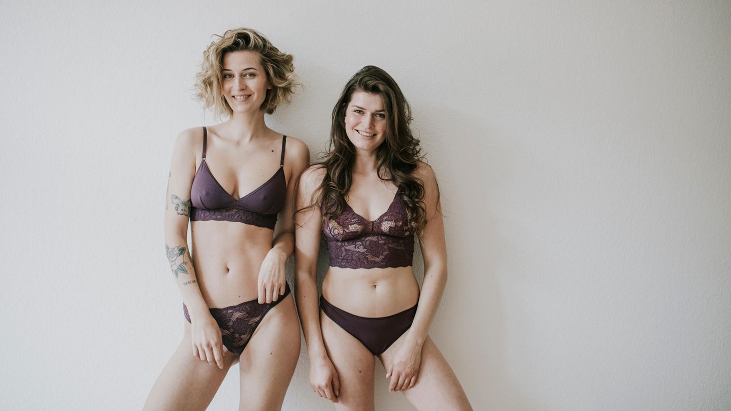 Zwei Frauen stehen in lila Unterwäsche vor einer weißen Wand.