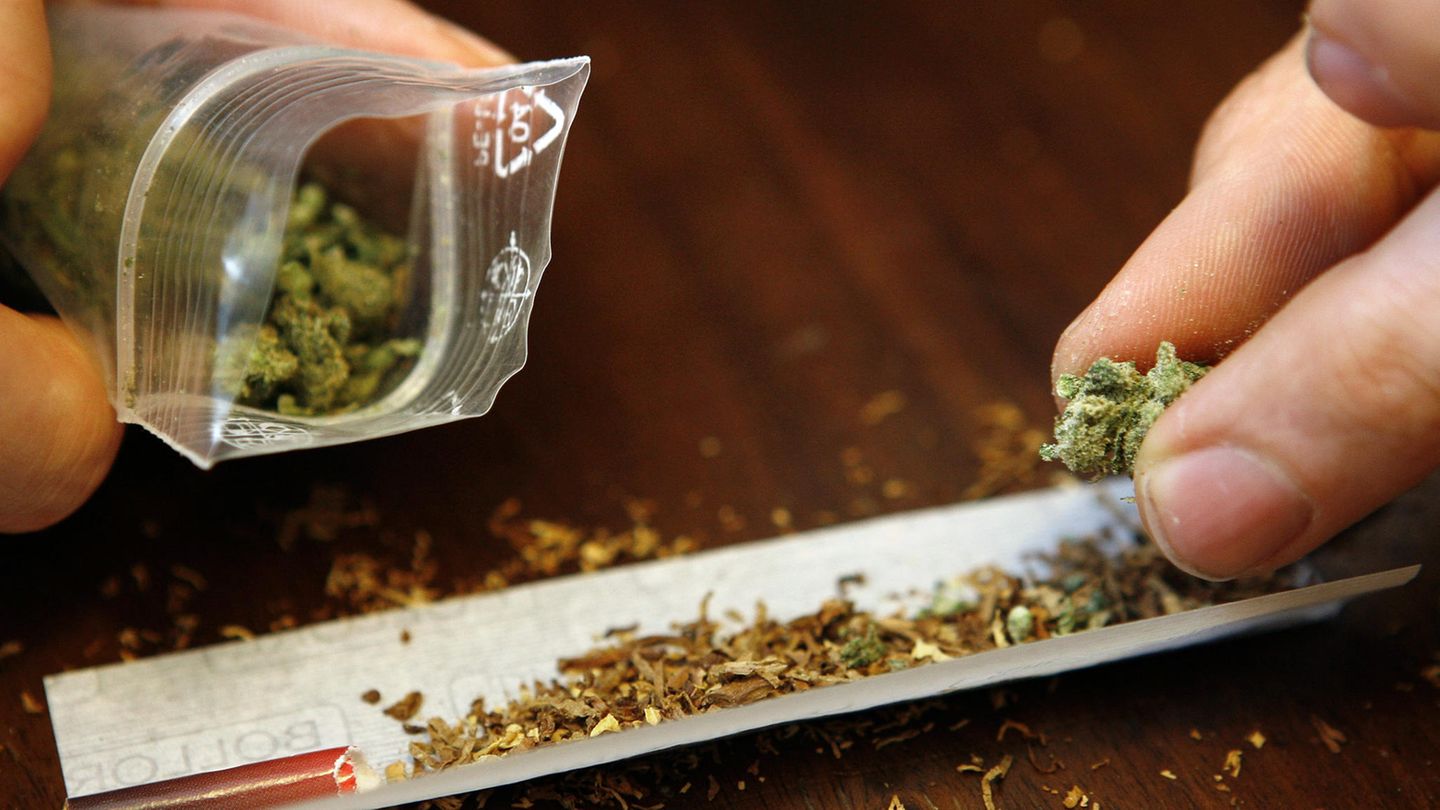 Ein Joint wird gedreht. Daneben wird eine kleine Tüte mit geringer Menge von Marihuana gehalten.
