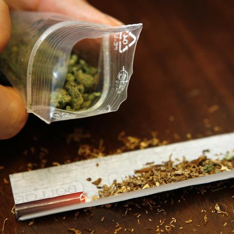 Ein Joint wird gedreht. Daneben wird eine kleine Tüte mit geringer Menge von Marihuana gehalten.
