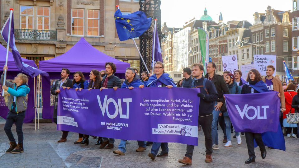 Mitglieder der Europa-Partei "Volt" ziehen mit Flaggen und Bannern in Amsterdam durch eine Straße.