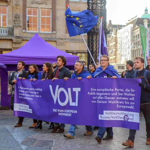 Mitglieder der Europa-Partei "Volt" ziehen mit Flaggen und Bannern in Amsterdam durch eine Straße.