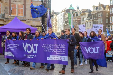 Mitglieder der Europa-Partei "Volt" ziehen mit Flaggen und Bannern in Amsterdam durch eine Straße.