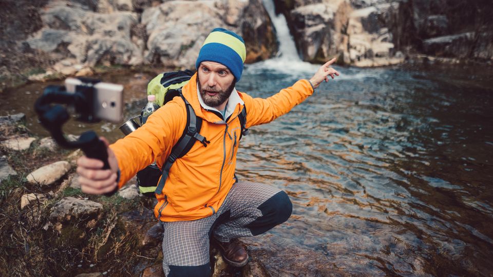 Ein Wanderer filmt sich selbst vor einem Wasserfall