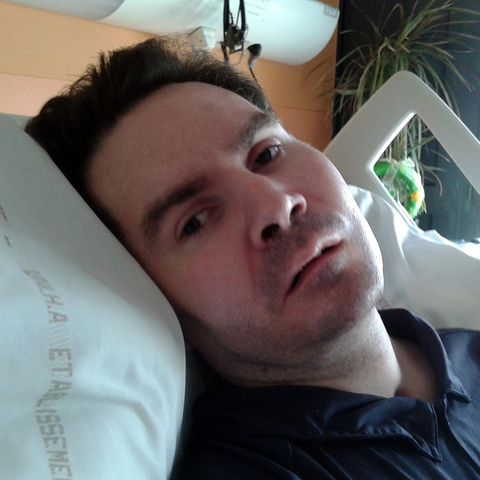 Eine Mann Ende 30 liegt in einem Krankenhausbett. Sein Kopf mit braunem Haar ist in die Kamera gedreht