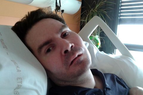 Eine Mann Ende 30 liegt in einem Krankenhausbett. Sein Kopf mit braunem Haar ist in die Kamera gedreht