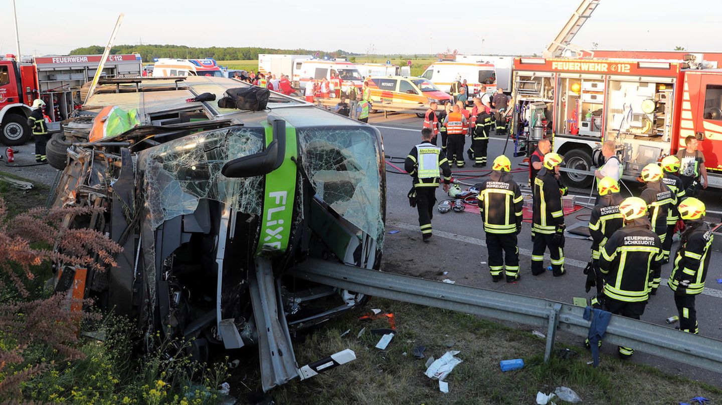 Einsatzkräfte der Feuerwehr stehen an der Unfallstelle auf der Autobahn 9 nahe Leipzig neben dem verunglückten Flixbus