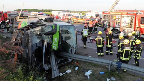 Einsatzkräfte der Feuerwehr stehen an der Unfallstelle auf der Autobahn 9 nahe Leipzig neben dem verunglückten Flixbus