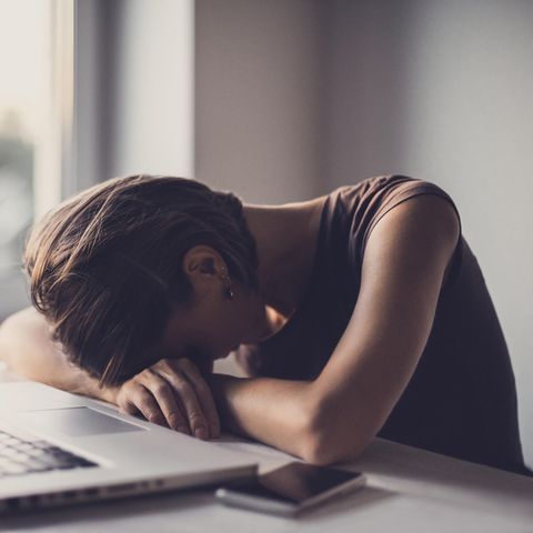 Frau liegt mit Kopf auf dem Tisch vor einem Laptop