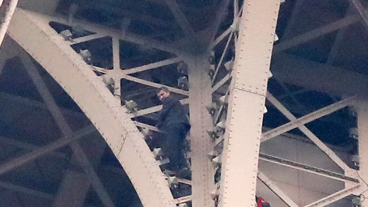 Ein Kletterer steht auf Eisenstreben hoch oben am Eifelturm