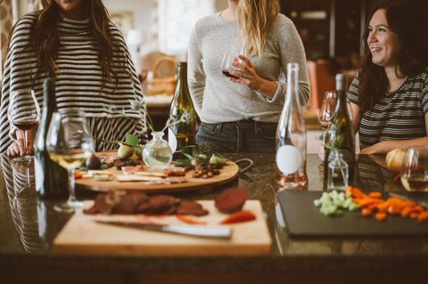 Frauen sitzen und stehen um Tisch und trinken Wein