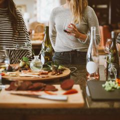 Frauen sitzen und stehen um Tisch und trinken Wein
