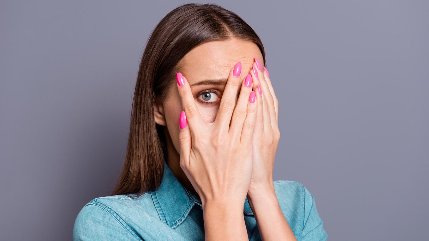 Eine Frau mit braunen Haaren hält sich die Hände vor die Augen und späht durch zwei Finger