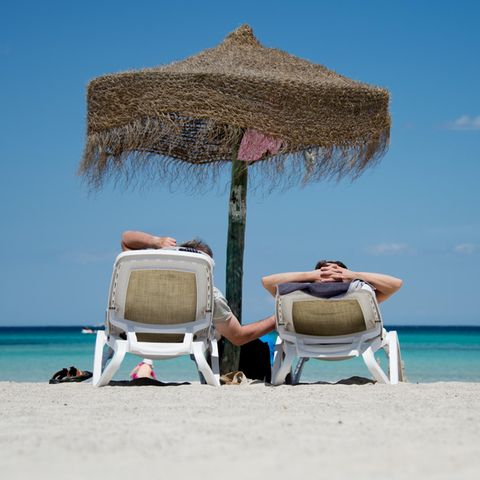 Zwei Urlauber liegen am Strand unter einem Sonnenschirm