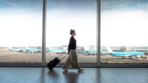 Frau geht mit einem Rollkoffer durch eine Flughafenhalle