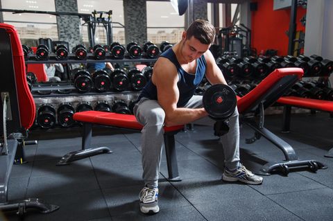Mann sitzt mit Hantel in einem Fitnessstudio.