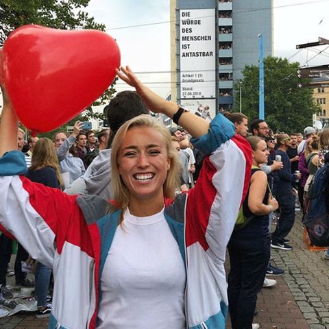 Blondes Mädchen in einer Menschenmenge mit einem herzförmigen Luftballon in der Hand.