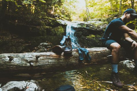 Ein Mann sitzt auf Baumstamm mit Wanderschuhen