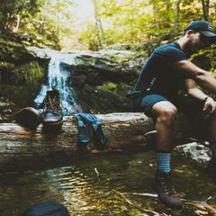 Ein Mann sitzt auf Baumstamm mit Wanderschuhen