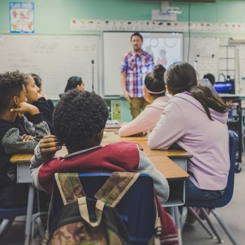 Kinder, die in einem Klassenzimmer sitzen. Sie schauen einen Lehrer an.
