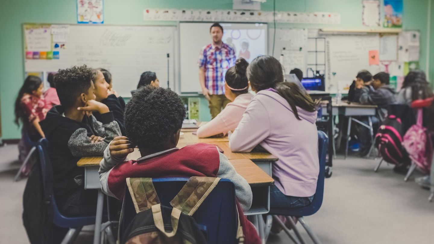 Kinder, die in einem Klassenzimmer sitzen. Sie schauen einen Lehrer an.