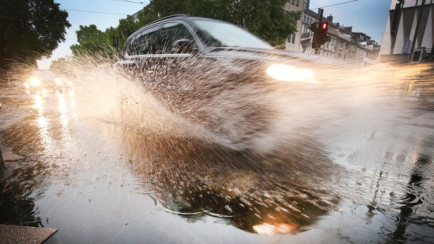 Aus einer Pfütze spritzt Wasser hoch, als ein Auto durchfährt