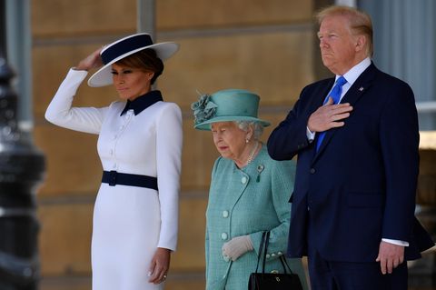 Die Hand gehört eigentlich nicht an den Hut: Melania Trump (l.) muss bei einem Windstoß nach oben greifen. Der Hut der Queen sitzt hingegen perfekt. Donald Trump bleibt unbeirrt.