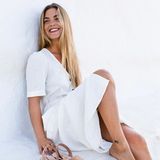 Frau in weißem Kleid hält ein Paar Espadrilles in der Hand.