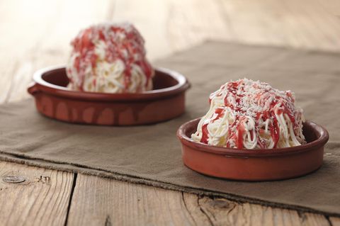 Spaghetti-Eis      Zutaten:  Für das Vanilleeis  1 Vanilleschote, 450 ml frische Vollmilch, 300 ml flüssige Sahne (32% Fettgehalt), 180 g Zucker, 120 g Eigelb (entspricht 6–7 Eigelb)  Spaghetti-Eis fertigstellen   200 ml flüssige Sahne, Erdbeersauce, geraspelte weiße Schokolade zum Garnieren  Außerdem: 1 Spätzlepresse      Zubereitung:  Vanille-Eis  Die Vanilleschote mit einem spitzen Messer der Länge nach aufschlitzen und mit dem Messerrücken das Mark herauskratzen. Die Milch, die Sahne, das Vanillemark und die leere Vanillesschote in einen Topf geben. Die Flüssigkeit aufkochen. Den Topf vom Herd ziehen und den Topfinhalt abkühlen lassen. Die Vanillemilch mit Folie bedecken und über Nacht im Kühlschrank durchziehen lassen. Die Vanillemilch erneut aufkochen, die Vanilleschote entfernen und den Topf beiseitestellen. In einer Rührschüssel die Eigelbe und den Zucker zu einer hellgelben, dickflüssigen Eiercreme aufschlagen. Die abgekühlte Vanillemilch unter die Eiercreme rühren. Diese Creme in einen Topf umfüllen und bei mittlerer Temperatur unter stetigem Rühren auf etwa 80°C (am besten ein Speisenthermometer verwenden) erhitzen, bis sie andickt. Achtung: Die Creme darf dabei keinesfalls kochen.  Den Topf mit der Vanillecreme auf ein Eiswasserbad stellen und abkühlen lassen. Die abgekühlte Creme in einen verschließbaren Becher füllen, diesen mit dem Deckel verschließen und im Kühlschrank gut durchkühlen lassen. Die Grundmasse in die Eismaschine umfüllen und nach den Angaben des Herstellers zu cremigem Eis verarbeiten. Das fertige Eis aus der Eismaschine nehmen und kurz im Gefrierfach fest werden lassen.      Spaghetti-Eis fertigstellen  Die Spätzlepresse und die Desserteller im Kühlschrank gut durchkühlen lassen. Die Sahne steif schlagen. Vor dem Servieren die Dessertteller aus dem Kühlschrank nehmen und jeweils 2–3 EL geschlagene Sahne darauf verteilen. Pro Teller 3 Kugeln Vanilleeis in die gekühlte Spätzlepresse geben und auf die Sahne drücken. Das Erdbeertopping darüber verteilen und mit den Schokoladenraspeln dekorieren. Sofort servieren.