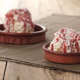 Spaghetti-Eis      Zutaten:  Für das Vanilleeis  1 Vanilleschote, 450 ml frische Vollmilch, 300 ml flüssige Sahne (32% Fettgehalt), 180 g Zucker, 120 g Eigelb (entspricht 6–7 Eigelb)  Spaghetti-Eis fertigstellen   200 ml flüssige Sahne, Erdbeersauce, geraspelte weiße Schokolade zum Garnieren  Außerdem: 1 Spätzlepresse      Zubereitung:  Vanille-Eis  Die Vanilleschote mit einem spitzen Messer der Länge nach aufschlitzen und mit dem Messerrücken das Mark herauskratzen. Die Milch, die Sahne, das Vanillemark und die leere Vanillesschote in einen Topf geben. Die Flüssigkeit aufkochen. Den Topf vom Herd ziehen und den Topfinhalt abkühlen lassen. Die Vanillemilch mit Folie bedecken und über Nacht im Kühlschrank durchziehen lassen. Die Vanillemilch erneut aufkochen, die Vanilleschote entfernen und den Topf beiseitestellen. In einer Rührschüssel die Eigelbe und den Zucker zu einer hellgelben, dickflüssigen Eiercreme aufschlagen. Die abgekühlte Vanillemilch unter die Eiercreme rühren. Diese Creme in einen Topf umfüllen und bei mittlerer Temperatur unter stetigem Rühren auf etwa 80°C (am besten ein Speisenthermometer verwenden) erhitzen, bis sie andickt. Achtung: Die Creme darf dabei keinesfalls kochen.  Den Topf mit der Vanillecreme auf ein Eiswasserbad stellen und abkühlen lassen. Die abgekühlte Creme in einen verschließbaren Becher füllen, diesen mit dem Deckel verschließen und im Kühlschrank gut durchkühlen lassen. Die Grundmasse in die Eismaschine umfüllen und nach den Angaben des Herstellers zu cremigem Eis verarbeiten. Das fertige Eis aus der Eismaschine nehmen und kurz im Gefrierfach fest werden lassen.      Spaghetti-Eis fertigstellen  Die Spätzlepresse und die Desserteller im Kühlschrank gut durchkühlen lassen. Die Sahne steif schlagen. Vor dem Servieren die Dessertteller aus dem Kühlschrank nehmen und jeweils 2–3 EL geschlagene Sahne darauf verteilen. Pro Teller 3 Kugeln Vanilleeis in die gekühlte Spätzlepresse geben und auf die Sahne drücken. Das Erdbeertopping darüber verteilen und mit den Schokoladenraspeln dekorieren. Sofort servieren.