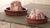 Spaghetti-Eis      Zutaten:  Für das Vanilleeis  1 Vanilleschote, 450 ml frische Vollmilch, 300 ml flüssige Sahne (32% Fettgehalt), 180 g Zucker, 120 g Eigelb (entspricht 6–7 Eigelb)  Spaghetti-Eis fertigstellen   200 ml flüssige Sahne, Erdbeersauce, geraspelte weiße Schokolade zum Garnieren  Außerdem: 1 Spätzlepresse      Zubereitung:  Vanille-Eis  Die Vanilleschote mit einem spitzen Messer der Länge nach aufschlitzen und mit dem Messerrücken das Mark herauskratzen. Die Milch, die Sahne, das Vanillemark und die leere Vanillesschote in einen Topf geben. Die Flüssigkeit aufkochen. Den Topf vom Herd ziehen und den Topfinhalt abkühlen lassen. Die Vanillemilch mit Folie bedecken und über Nacht im Kühlschrank durchziehen lassen. Die Vanillemilch erneut aufkochen, die Vanilleschote entfernen und den Topf beiseitestellen. In einer Rührschüssel die Eigelbe und den Zucker zu einer hellgelben, dickflüssigen Eiercreme aufschlagen. Die abgekühlte Vanillemilch unter die Eiercreme rühren. Diese Creme in einen Topf umfüllen und bei mittlerer Temperatur unter stetigem Rühren auf etwa 80°C (am besten ein Speisenthermometer verwenden) erhitzen, bis sie andickt. Achtung: Die Creme darf dabei keinesfalls kochen.  Den Topf mit der Vanillecreme auf ein Eiswasserbad stellen und abkühlen lassen. Die abgekühlte Creme in einen verschließbaren Becher füllen, diesen mit dem Deckel verschließen und im Kühlschrank gut durchkühlen lassen. Die Grundmasse in die Eismaschine umfüllen und nach den Angaben des Herstellers zu cremigem Eis verarbeiten. Das fertige Eis aus der Eismaschine nehmen und kurz im Gefrierfach fest werden lassen.      Spaghetti-Eis fertigstellen  Die Spätzlepresse und die Desserteller im Kühlschrank gut durchkühlen lassen. Die Sahne steif schlagen. Vor dem Servieren die Dessertteller aus dem Kühlschrank nehmen und jeweils 2–3 EL geschlagene Sahne darauf verteilen. Pro Teller 3 Kugeln Vanilleeis in die gekühlte Spätzlepresse geben und auf die Sahne drücken. Das Erdbeertopping darüber verteilen und mit den Schokoladenraspeln dekorieren. Sofort servieren.