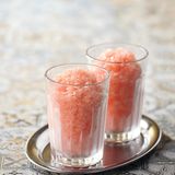 Wassermelonen-Granita      Zutaten:  100 g Zucker, 1 mittelgroße Wassermelone, 2–3 Spritzer frisch gepresster Zitronensaft, Abrieb von 1 unbehandelten Zitrone (optional)      Zubereitung:  Den Zucker mit 100 ml Wasser in einen Topf geben, unter Rühren aufkochen und etwa 10 Minuten köcheln lassen, bis sich der Zucker aufgelöst hat. Den Zuckersirup abkühlen lassen und im Kühlschrank gut durchkühlen. Die Wassermelone halbieren und das Fruchtfleisch aus der Schale schneiden. Dabei sorgfältig alle Kerne entfernen. Das Fruchtfleisch in grobe Stücke zerkleinern. Es werden 600 g reines Fruchtfleisch benötigt – diese Menge abwiegen und in einen Mixbecher mit hohem Rand geben. Das Wassermelonenfleisch mit dem Stabmixer pürieren. Den Zuckersirup, den Zitronensaft und gegebenenfalls den Zitronenabrieb unter das Wassermelonenpüree rühren. Diese Granita-Grundmasse in eine flache Gefrierbox füllen, sodass die Füllhöhe 3–4 cm nicht übersteigt. Die Form mit dem Deckel verschließen und waagerecht in den Gefrierschrank stellen. Im Abstand von je 30 Minuten mit einer Gabel alle Eiskristalle, die sich am Boden und an der Wand der Form gebildet haben, zur Mitte hin zusammenschieben. Nach etwa 3 Stunden sollte die gesamte Menge durchgefroren sein, die Granita ist dann servierfertig. Zum Servieren die Granita mit einem großen Löffel von der Oberfläche schaben und anrichten.