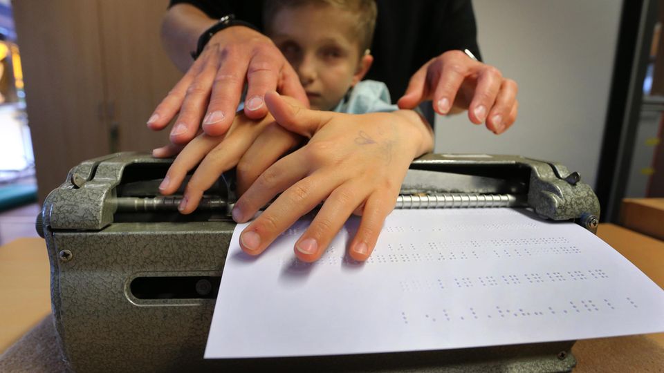 Der taubblinde Lucas ertastet, unterstützt von seiner Erzieherin Stefanie Tröster, Buchstaben in Blindenschrift