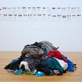 Auf dem Boden liegt ein Stapel Kleidung, an der Wänden hängen Berichte von Frauen mit Fotos