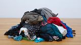 Auf dem Boden liegt ein Stapel Kleidung, an der Wänden hängen Berichte von Frauen mit Fotos