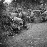 Alliierte Soldaten suchen Schutz hinter Wall und Hecke.