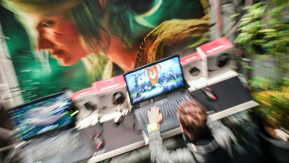 Ein Junge spielt ein Computerspiel, er sitzt vor einer Wand, auf die der Kopf einer Frau gemalt ist