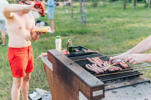 Mann mit roter Badehose hält Hotdog