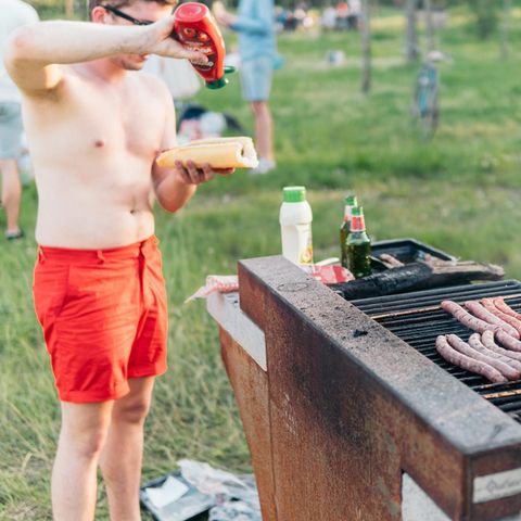 Mann mit roter Badehose hält Hotdog